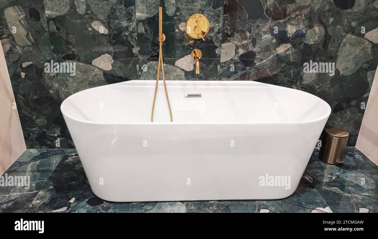 Ceramic bathtub in bathroom with gold faucets and green marble tiles