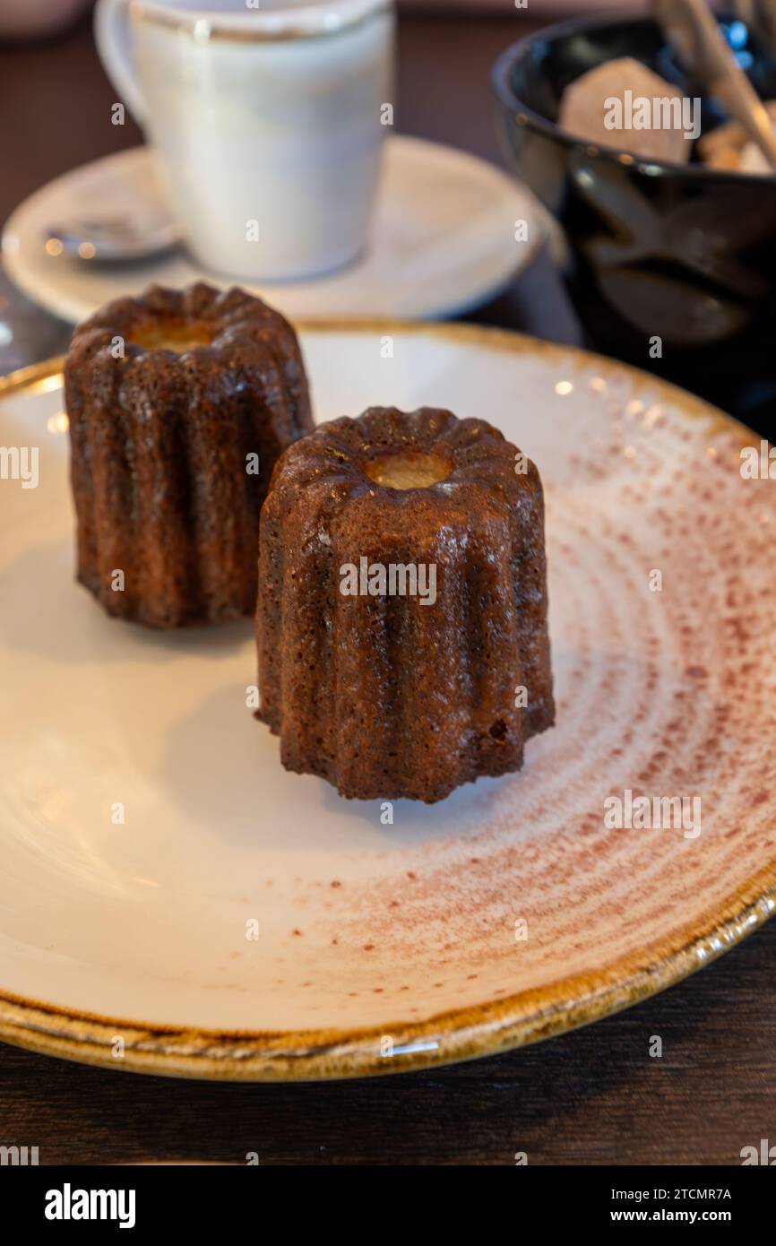 Canele, French pastry flavored with rum and vanilla, specialty of Bordeaux region, France, served on white plate with cup of black coffie in French re Stock Photo