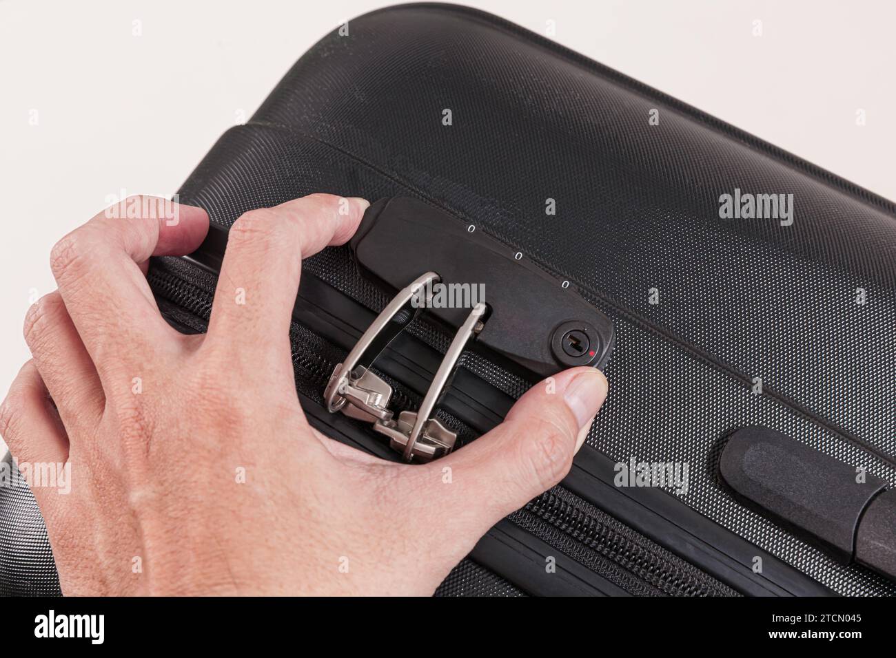 Hand opens lock on black plastic suitcase isolated on white background Stock Photo