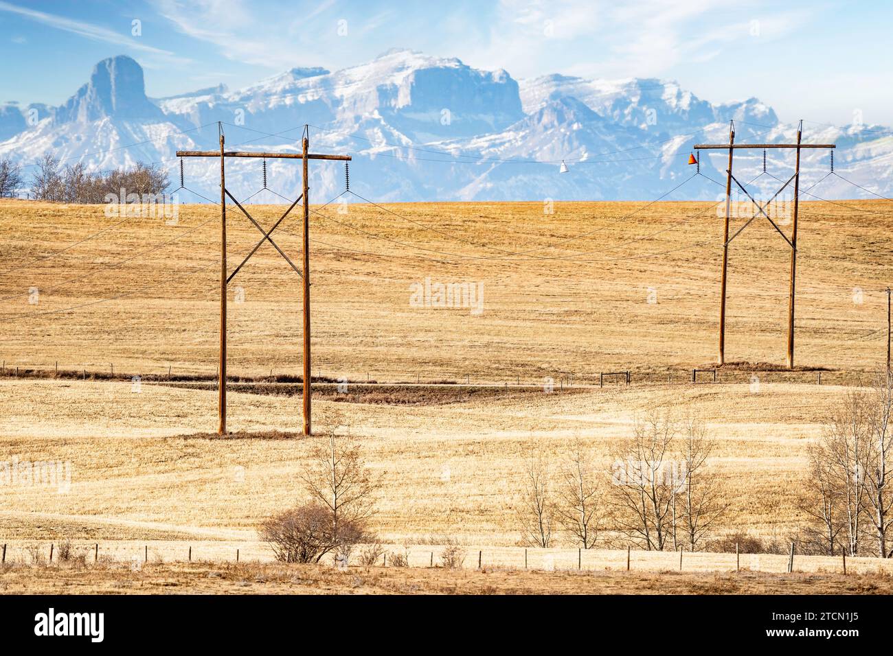 Pair of large wooden power poles with hanging electrical wires overlooking a hilltop and the distant Canadian Rocky Mountains near Cochrane Alberta Ca Stock Photo