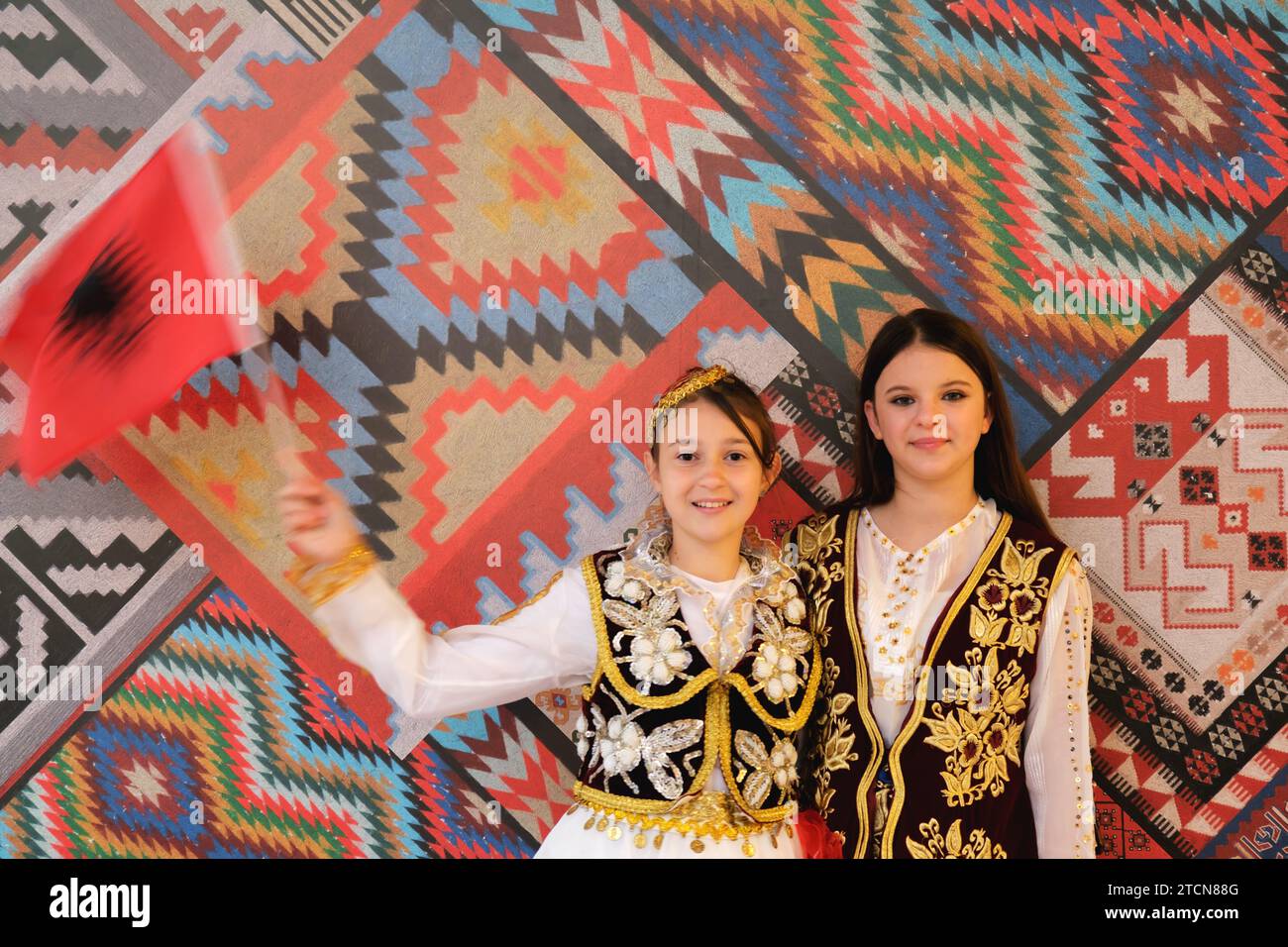 Tirana, Albania - November 28: Two girls with Albanian flags pose in front of traditional patterns at Palace of Congresses during Independence Day Stock Photo