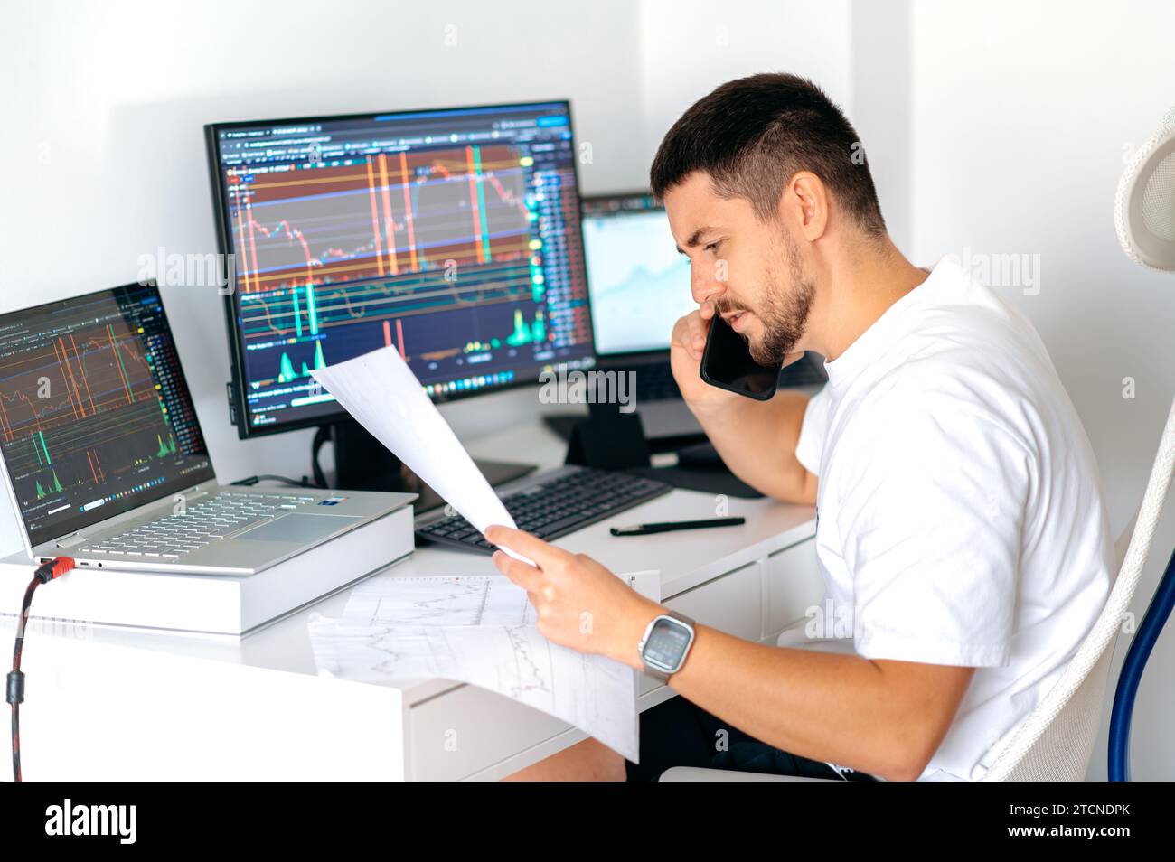 Busy caucasian male crypto trader sitting at home at his work desk in front  of monitors