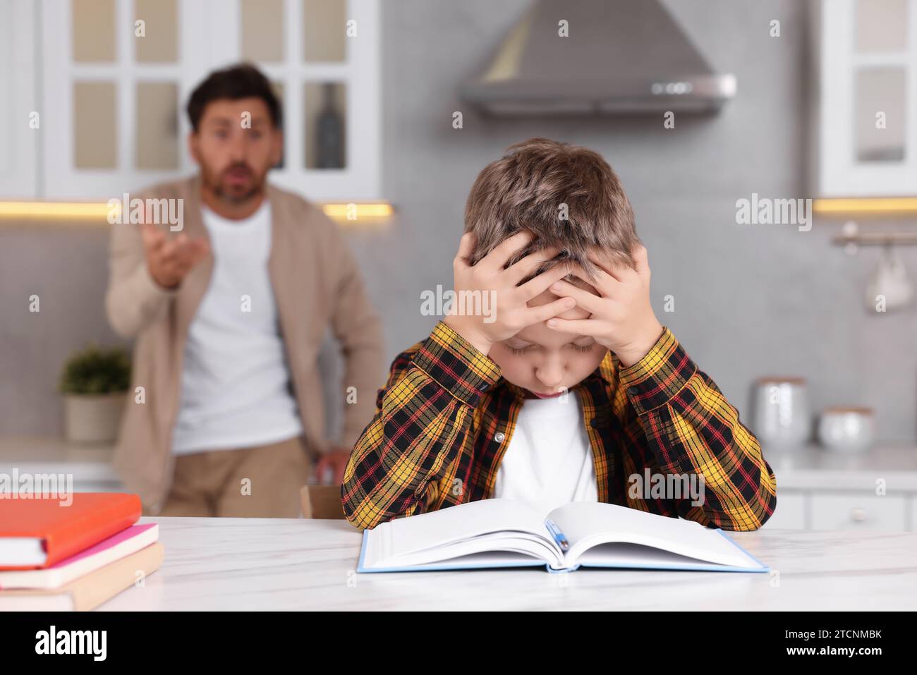 Father getting annoyed while son doing his homework in kitchen, selective focus. Dyslexia problem Stock Photo