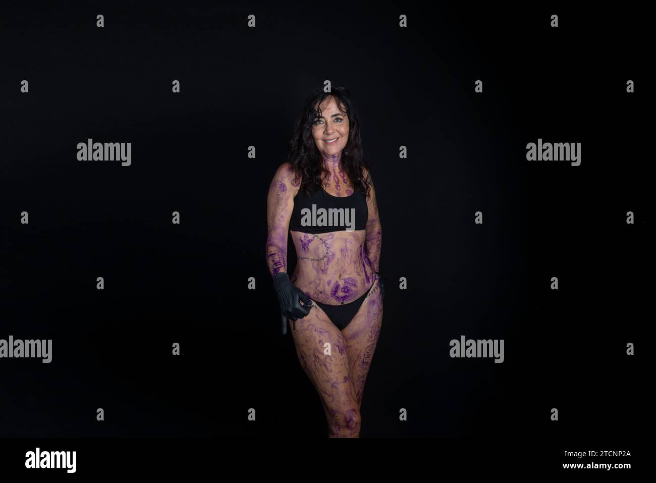 Beautiful woman wearing black bikini with painted and tattooed body against black background. Stock Photo