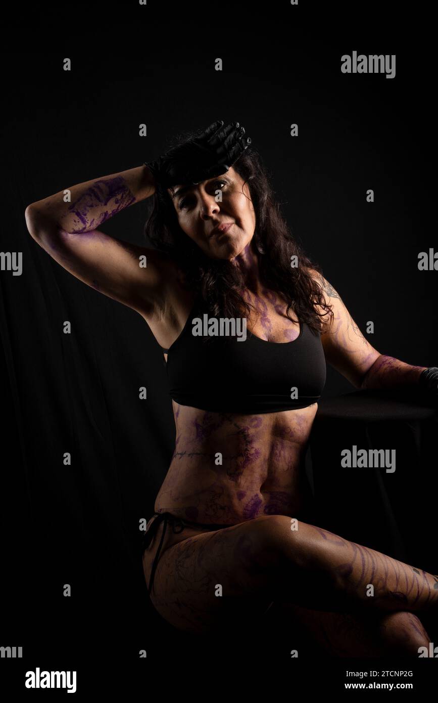 Tattooed artist, sitting, with painted and tattooed body against black background Stock Photo