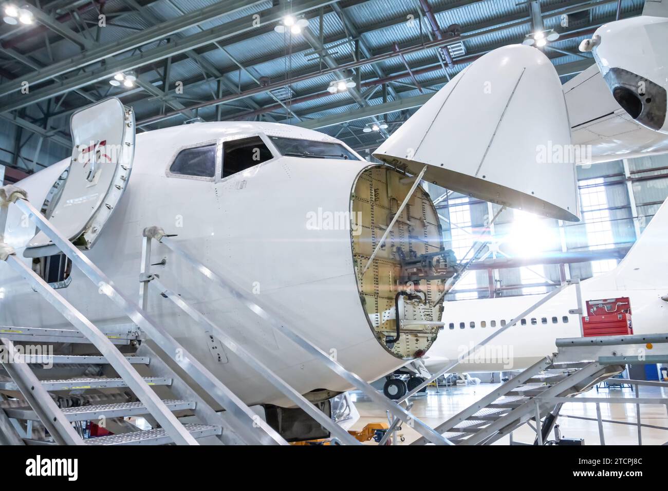 Front view of the white passenger airlines under maintenance in the aviation hangar. The jetliner has opened weather radar. Checking mechanical system Stock Photo