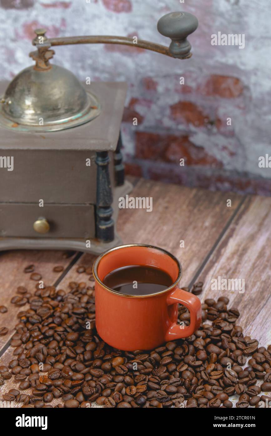 Red coffee cup on a pile of coffee beans and an antique manual coffee grinder in the background Stock Photo