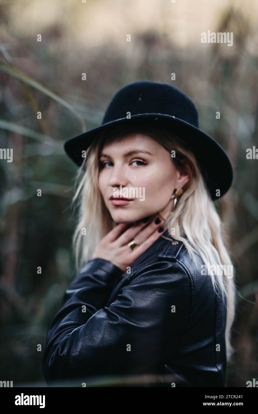 Blonde girl in a leather jacket and hat posing against the background of a field Stock Photo