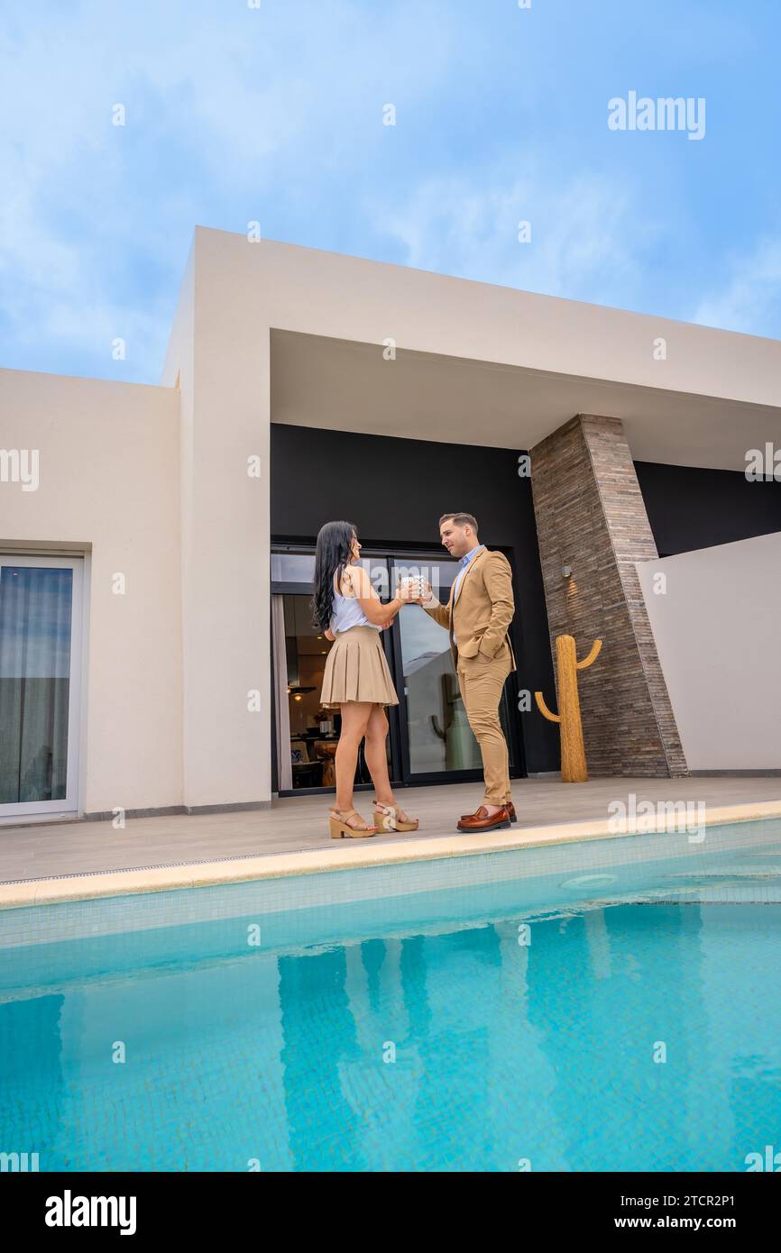Vertical photo of a couple toasting int he patio of their new luxury house next to the pool Stock Photo