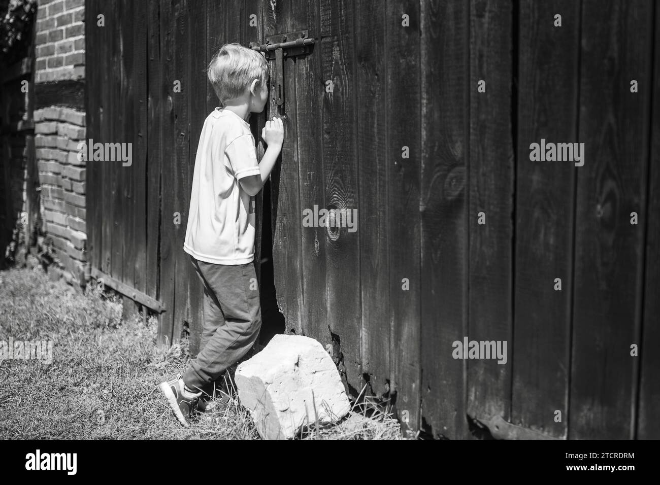 Children's curiosity - boy looking throw the hol in the gate to the shed Stock Photo