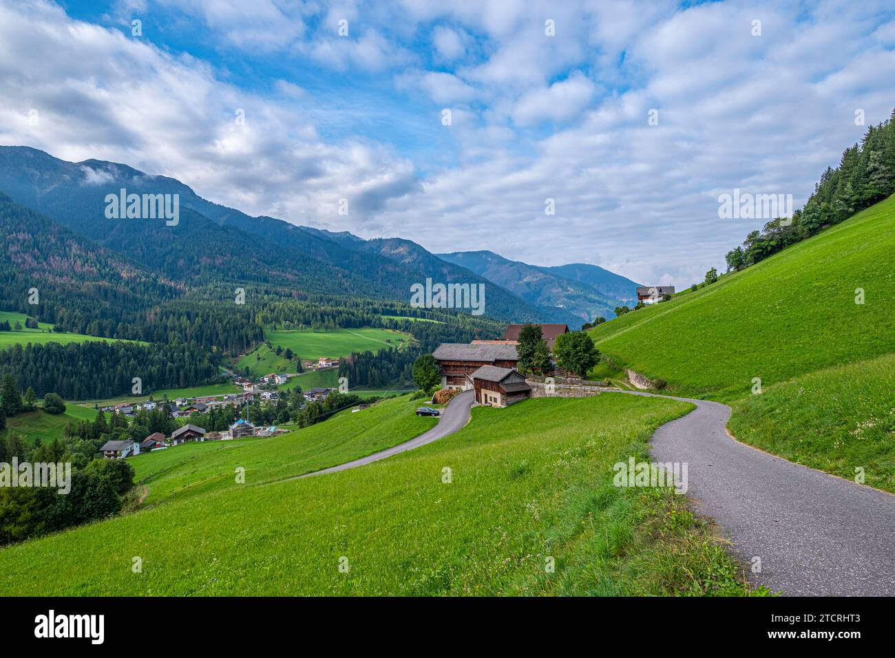 Santa Maddalena, Val di Funes, Quaint house along a winding road, framed by lush pastures, leading to the majesty of layered Dolomites, an enchanting Stock Photo