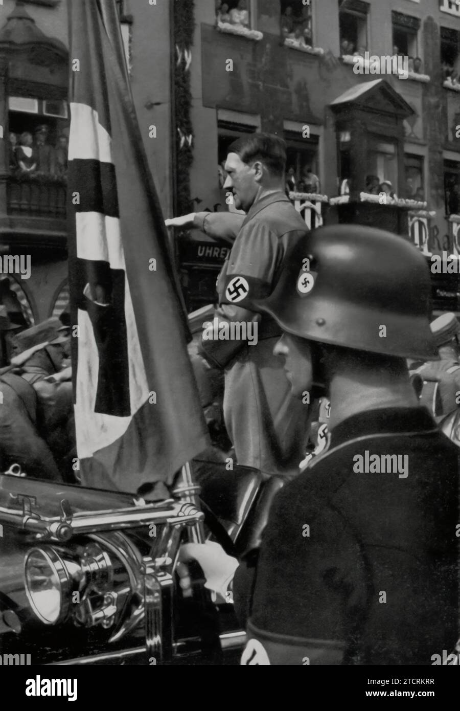 At the Nuremberg Rally, Adolf Hitler is seen saluting the 'Blutfahne' (Blood Flag) from 1923, a revered symbol in Nazi lore. This flag, stained with the blood of party members from the Beer Hall Putsch, was used to consecrate new flags. Hitler's salute to the Blutfahne underscores the regime's veneration of its early struggles and the sacrifices of its members, symbolizing a continuous thread of loyalty and martyrdom within the Nazi movement. Stock Photo