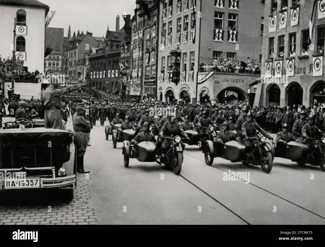 At the 1935 Reichsparteitag (Nazi Party Rally), Adolf Hitler is seen standing in his open-top car, saluting the motorized SA (Sturmabteilung) units. This image captures a moment of interaction between Hitler and the SA, emphasizing the role of motorization in the Nazi military apparatus. Hitler's salute from the car, a symbol of his leadership and the regime's modernization efforts, highlights the importance of the SA in the party's show of strength and unity during these large-scale, highly choreographed events. Stock Photo