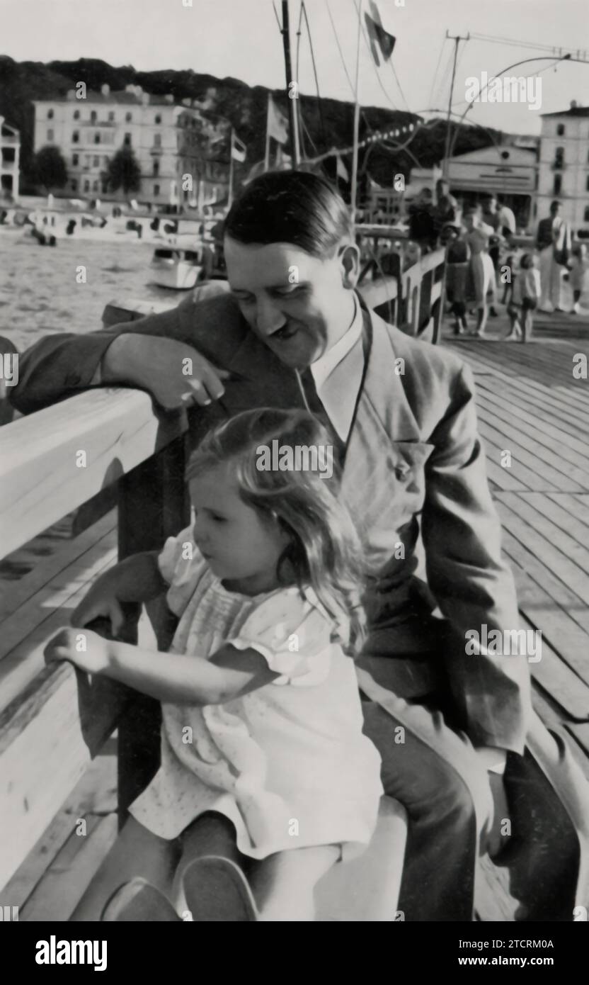 Adolf Hitler is captured in a moment of calm, accompanied by Helga Goebbels, the young daughter of Joseph Goebbels. This image contrasts with his typical public and political appearances, showing a more private side. The presence of Helga aims to present Hitler in a more relatable and softer light, a tactic used in Nazi propaganda to humanize him and portray him as a benevolent figure. Stock Photo