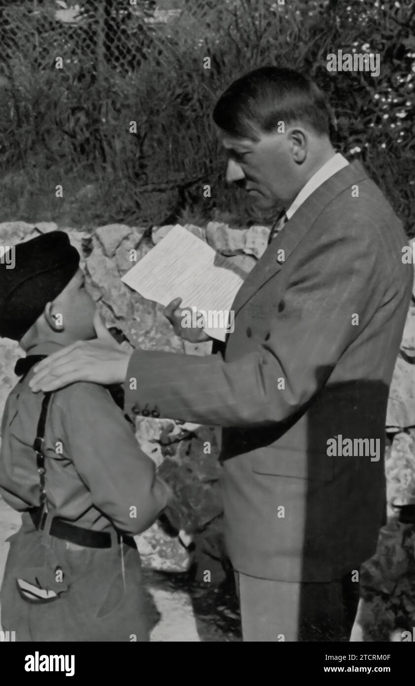 In this photograph, a young member of the Hitler Youth, known as a 'Pimpf,' is shown presenting a letter to Adolf Hitler, reportedly from his sick mother. The image captures a moment designed to reflect the perceived personal connection between Hitler and the youth of Germany. It also serves as a piece of propaganda, portraying Hitler as an accessible and caring figure, even to the youngest in society. The act of receiving a letter from a child's mother underscores the regime's attempt to project an image of Hitler as a leader involved in the personal lives of his people. Stock Photo