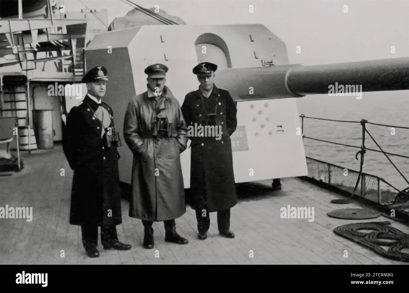 Adolf Hitler, standing on the deck of a warship in front of an artillery gun, during 'Besuch bei der Flotte' (Visit to the Fleet). This moment captures his engagement with the Kriegsmarine, the German Navy, highlighting his role in promoting the military's expansion and modernization, crucial elements of the Nazi regime's agenda. Stock Photo