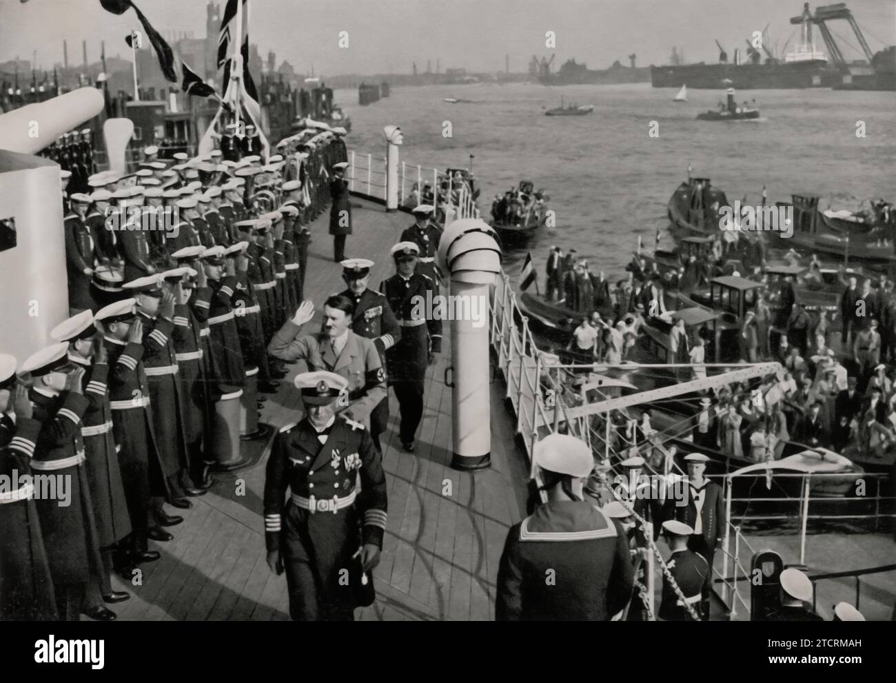 During Adolf Hitler's visit to the battleship Schleswig-Holstein in the Hamburg harbor, he is seen walking past the crew lined up on the deck. This moment captures the Führer's direct interaction with naval personnel, underscoring his role in the revitalization and promotion of the German Navy. The setting aboard the Schleswig-Holstein, a significant warship of the Kriegsmarine, highlights the importance of naval power in the broader context of military strategy and national pride in Nazi Germany. Stock Photo