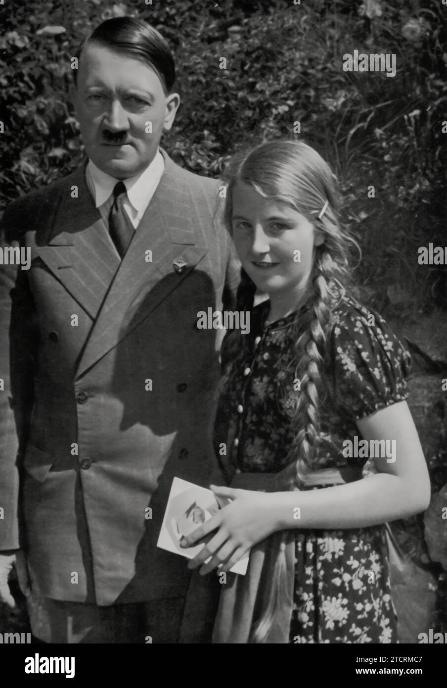 After receiving an autograph from Adolf Hitler, a young girl is fortunate enough to have her photograph taken with him. This image captures a personal and propagandistic moment, showcasing Hitler's interaction with the youth as part of the regime's efforts to portray him as a benevolent and approachable leader. Such staged encounters were instrumental in shaping public perception and fostering a sense of personal connection between Hitler and the German people, especially the younger generation. Stock Photo