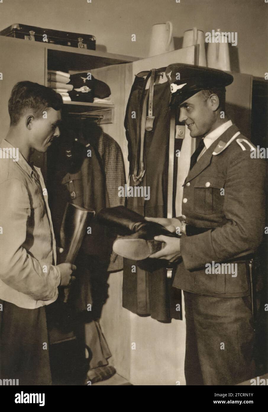 In the photograph, a German officer is seen conducting an inspection of a locker, likely belonging to a recruit in the Luftwaffe, the German Air Force. This practice of locker inspections was a routine yet vital aspect of military life, serving to reinforce discipline and order among the ranks. In the Luftwaffe, where precision and meticulousness were particularly valued, such inspections ensured that personal and issued equipment were kept in optimal condition and ready for use. Stock Photo