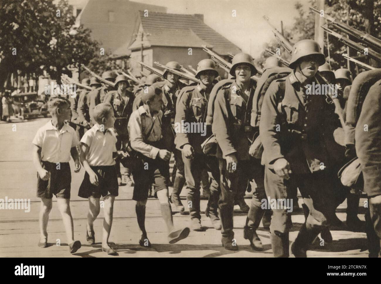 Children walk alongside the soldiers as they march into battle, a scene witnessed across various German regions. Their presence, with smiles and cheers, adds a poignant dimension to this moment of military unity, reflecting the widespread impact of the period on all ages. Stock Photo