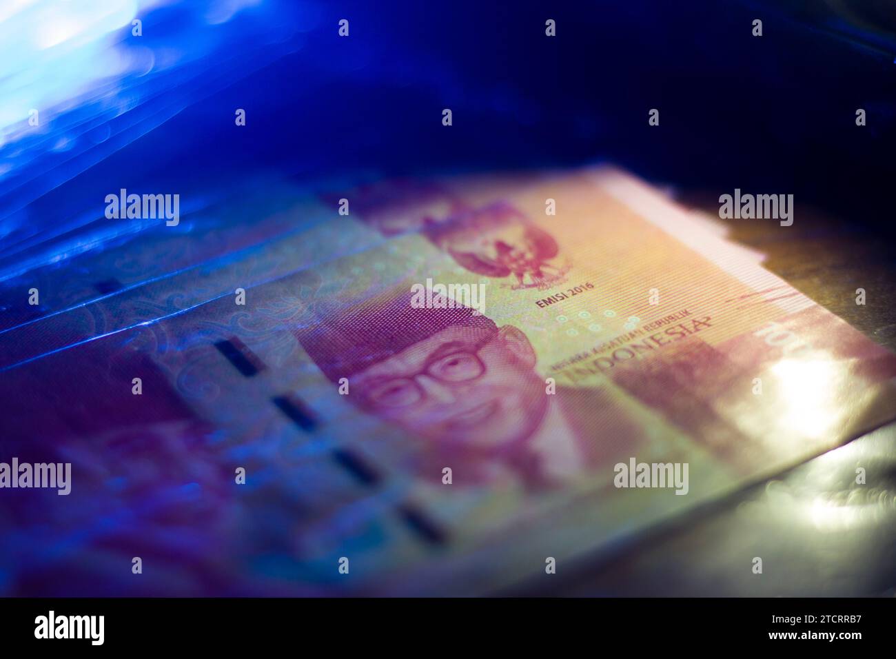 a stack of folded one hundred thousand rupiah banknotes Indonesian money selective focus dark blue lighting Stock Photo