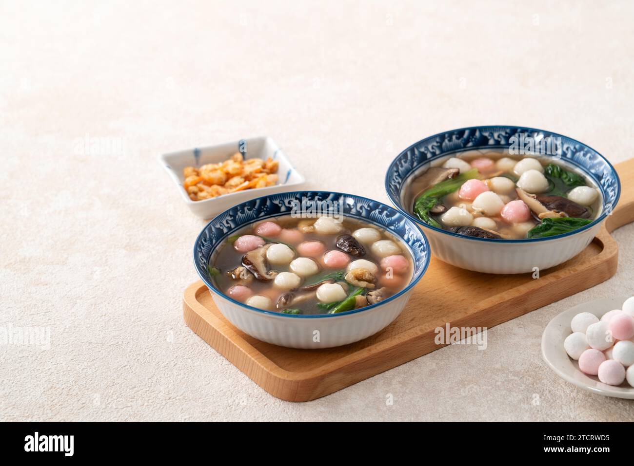 Eating red and white small tangyuan, tang yuan, glutinous rice dumpling balls with savory soup in a bowl on white table background. Stock Photo