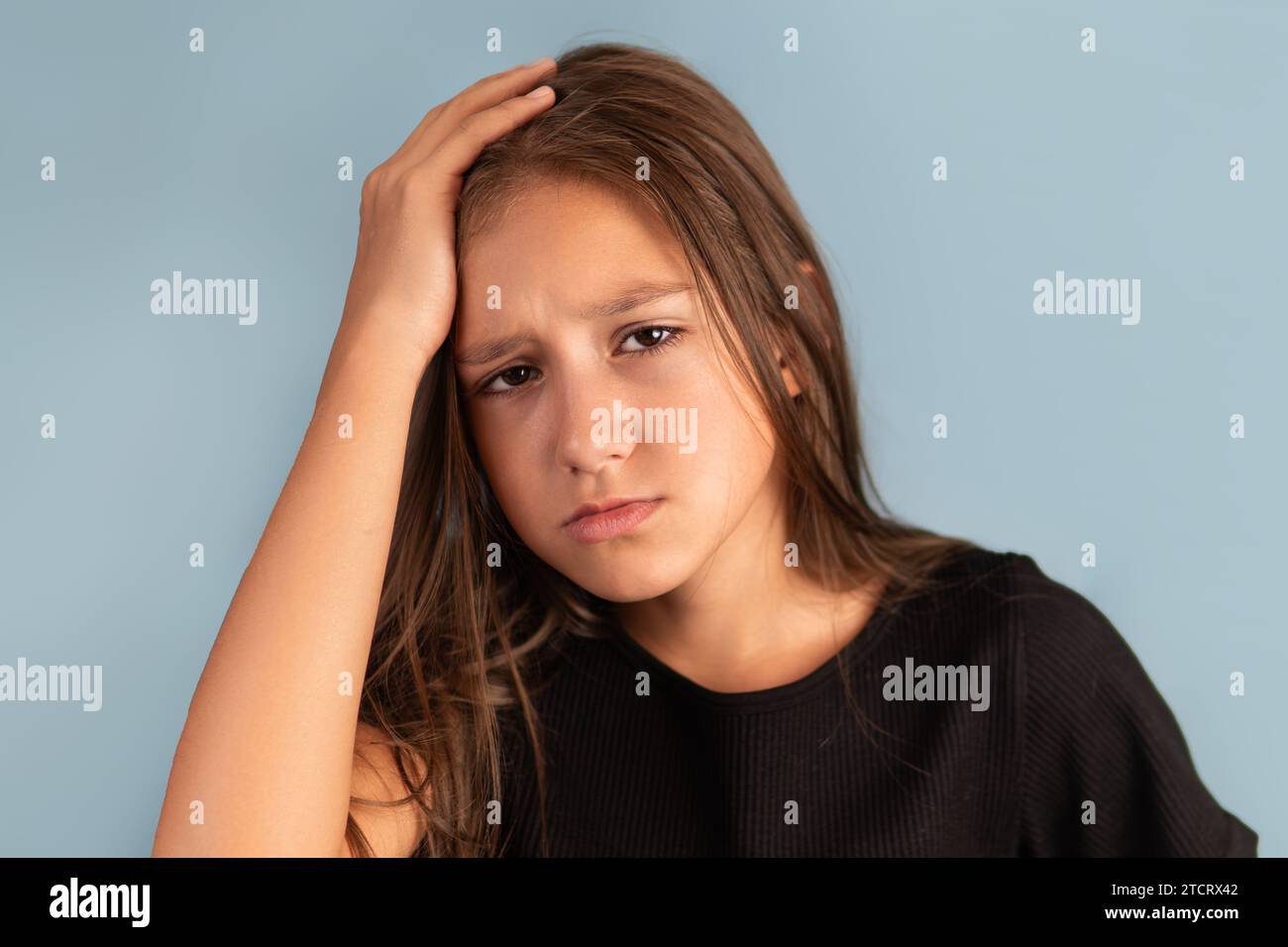 Little tired exhausted kid teen girl of 10-12 years old in black T-shirt put hand on forehead. look camera on pastel plain light blue background.. Stock Photo