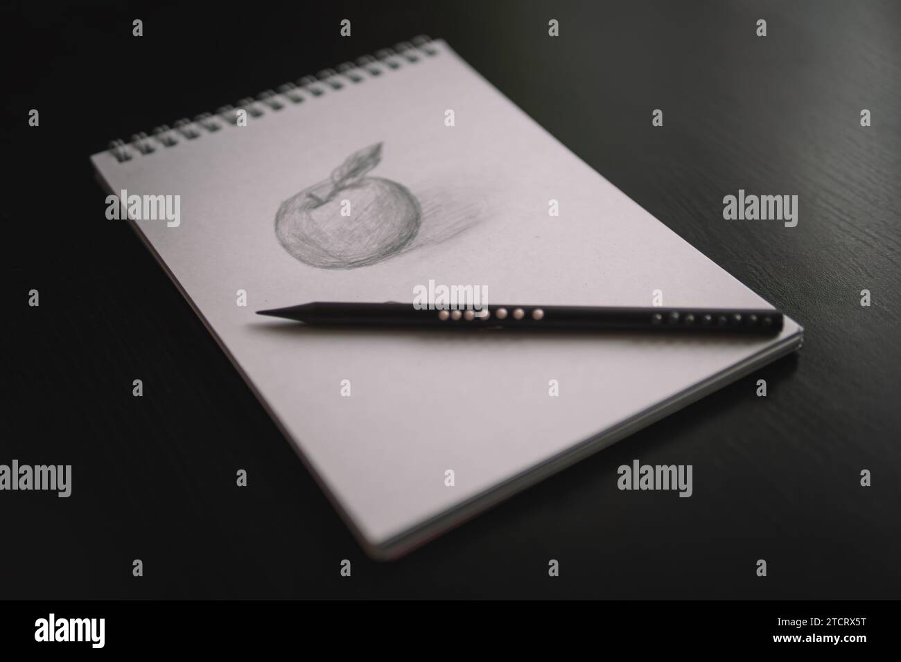 An apple pencil drawing in a notebook and a pencil on a black table. Learning to draw a concept. Stock Photo