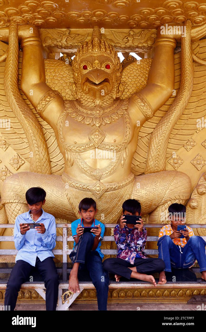 Mongkol Serei Kien Khleang Pagoda. Hindu deity. Golden Garuda statue. Children playing on a  smartphone.  Phnom Penh; Cambodia. Stock Photo