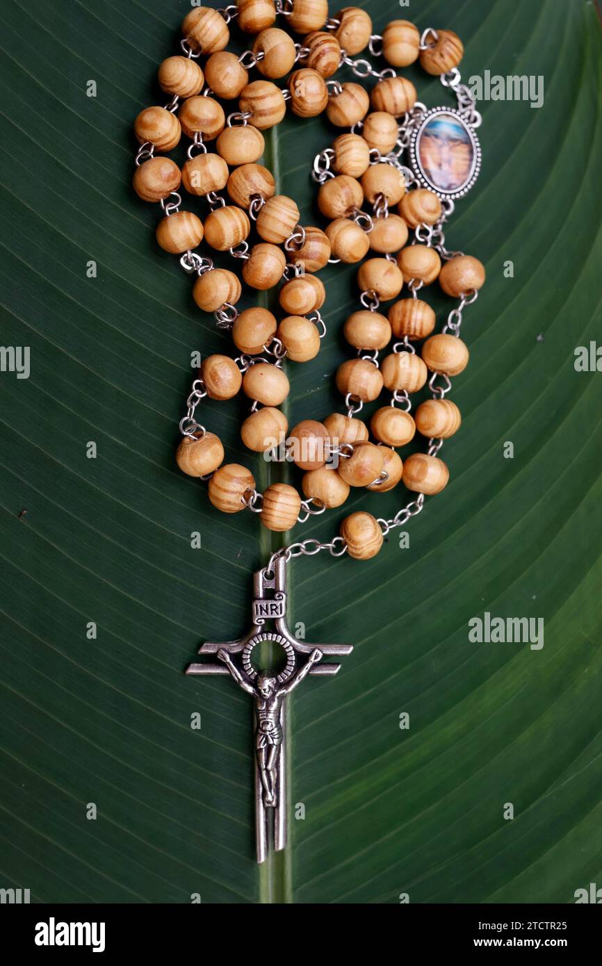 Rosary or prayer beads on a green leaf. Jesus on the cross. Crucifix. Stock Photo