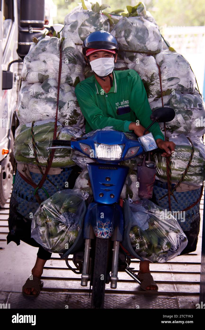 Vietnam car ferry on Mekong river near Chau Doc. Man with a lot of bags on motorbike. Stock Photo