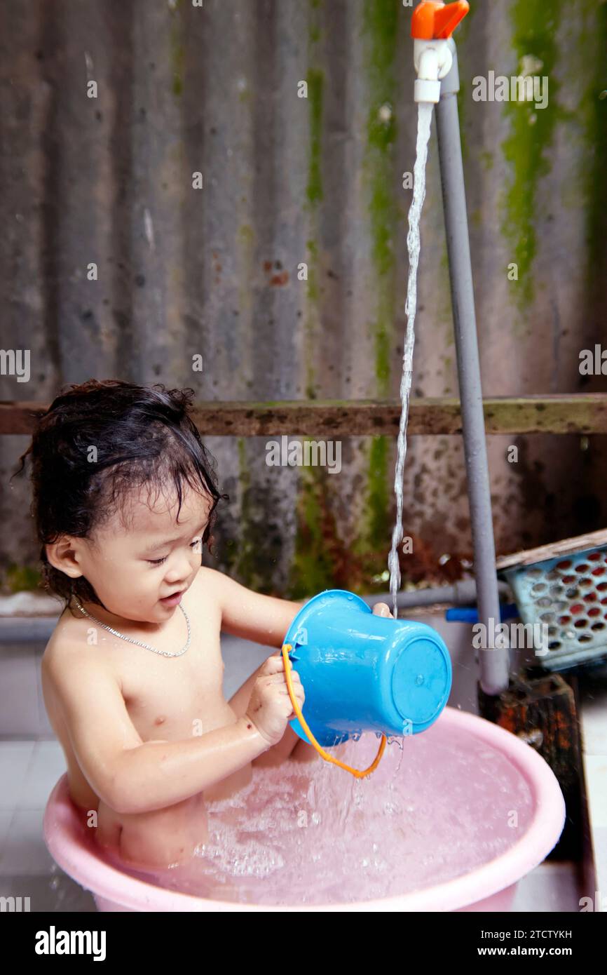 Little Vietnamese boy being bathed in a plastic basin. Stock Photo
