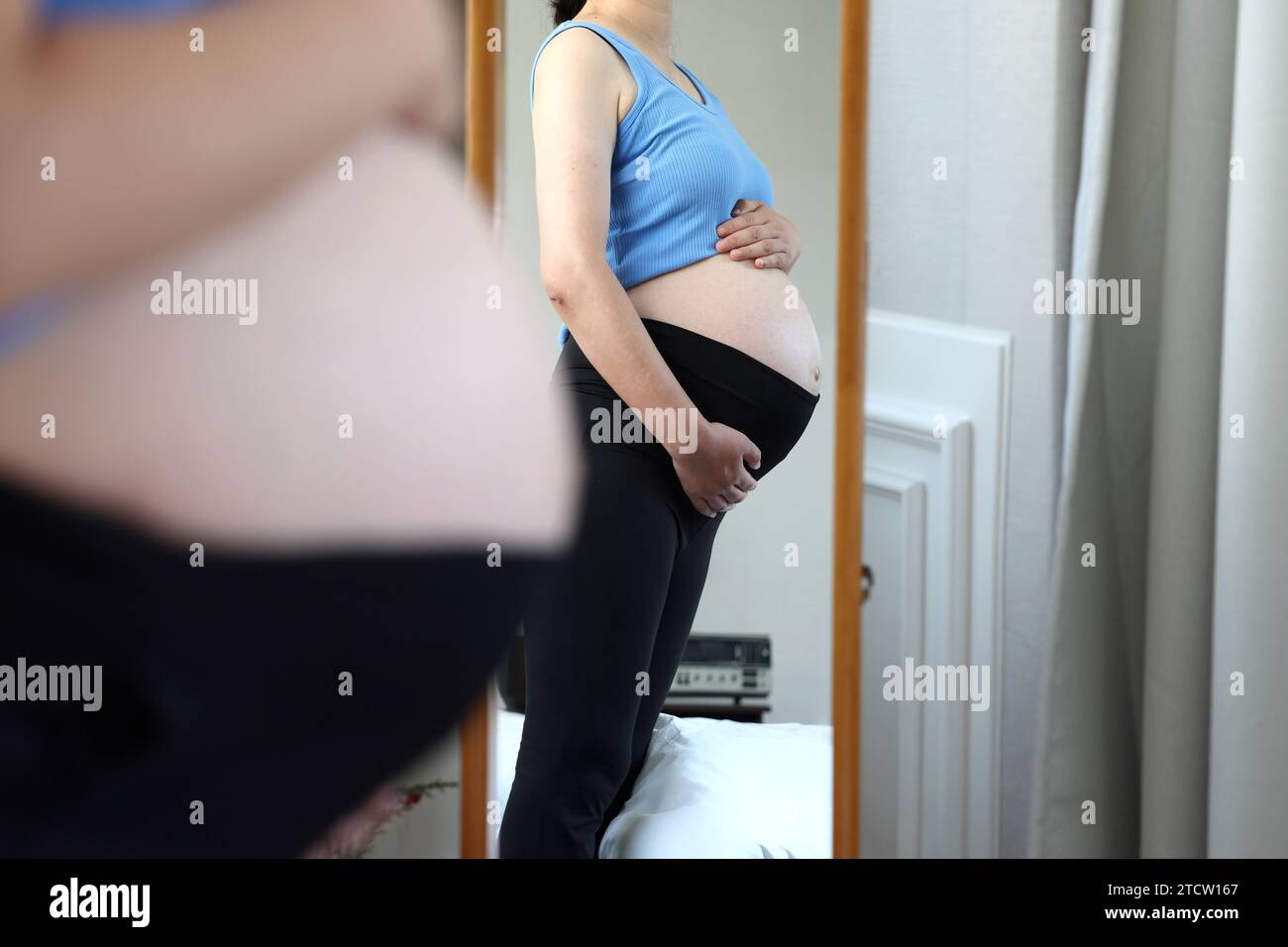Pregnant woman looking at her belly in front of a full-length mirror Stock Photo