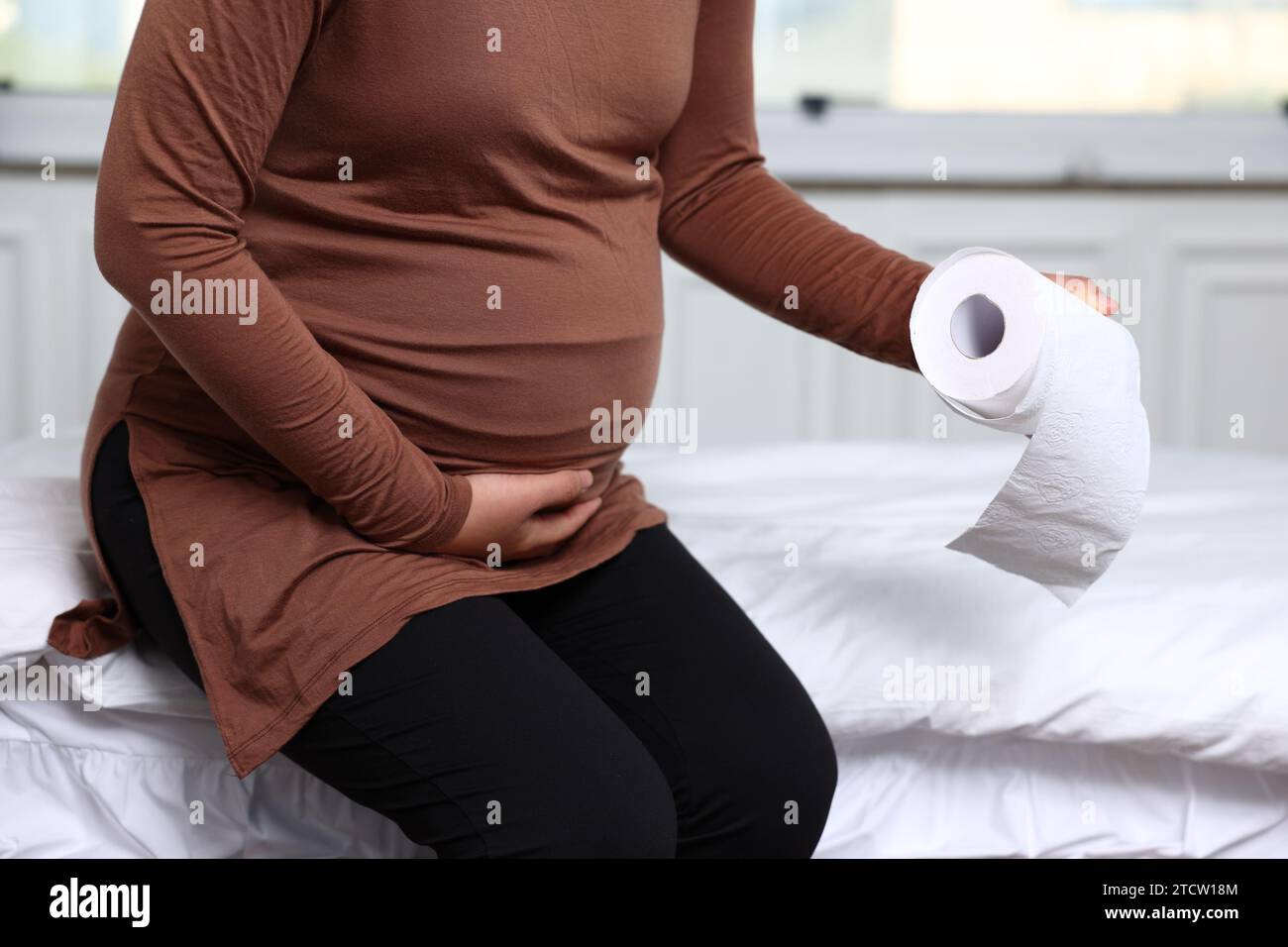 A pregnant woman waking up in the morning and holding a tissue in bed due to bowel