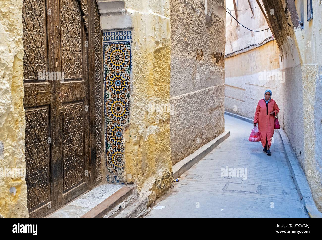 Beautiful carved wooden door and Muslim woman wearing djellaba / jillaba and hijab in alley of medina in the city Fes / Fez, Fez-Meknes, Morocco Stock Photo