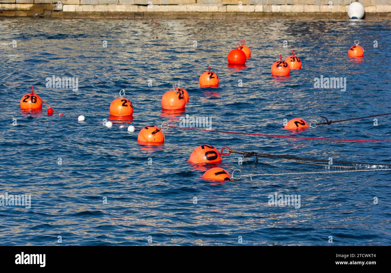 Group of numbered orange colored floating buoys in the seawater next to