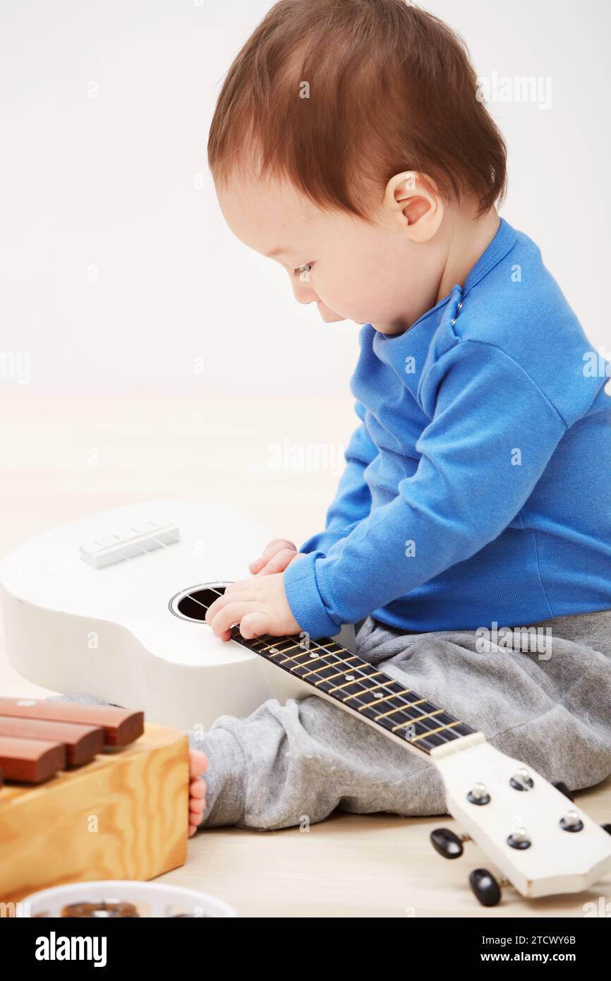 Baby, guitar toys and play in home for entertainment joy, childhood development or education. Boy, kid and instruments for musical strings for song Stock Photo