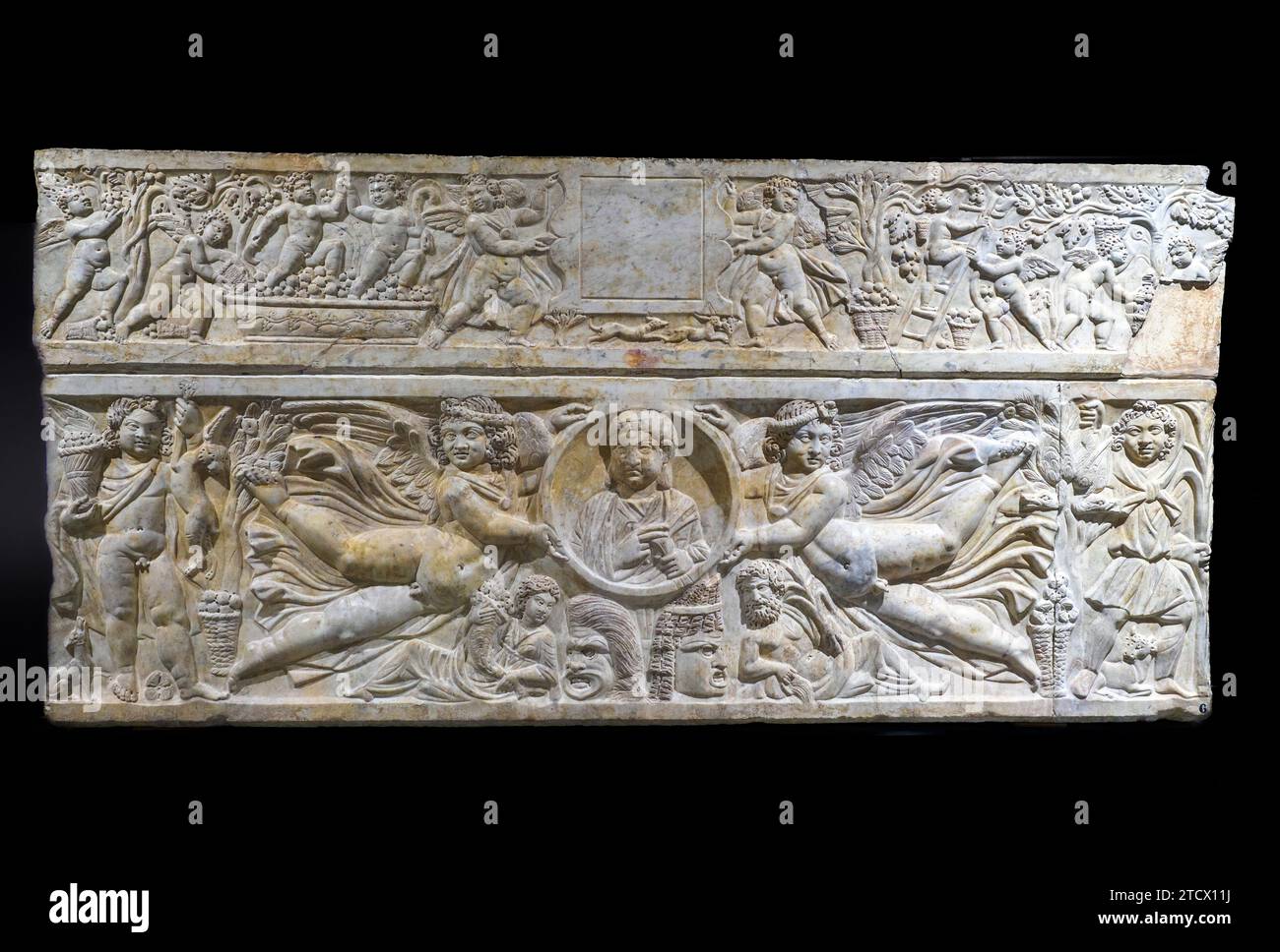 Sarcophagus with clipeus supported by winged Erotes;  Marble from Luni; End of third century AD. The portrait of the deceased, with a rotulus in her left hand, is in the center of the sarcophagus, inside a clypeus supported by winged Erotes. The sarcophagus is richly decorated: at the corners are two Genes, personifications of the seasons, while under the clipeus thare are two theatrical masks, on the sides of which the personifications of the Earth and the Oceanus are placed. Livelygrape-harvesting putti decorate the front side of the lid - Museo Centrale Montemartini, Rome, Italy Stock Photo