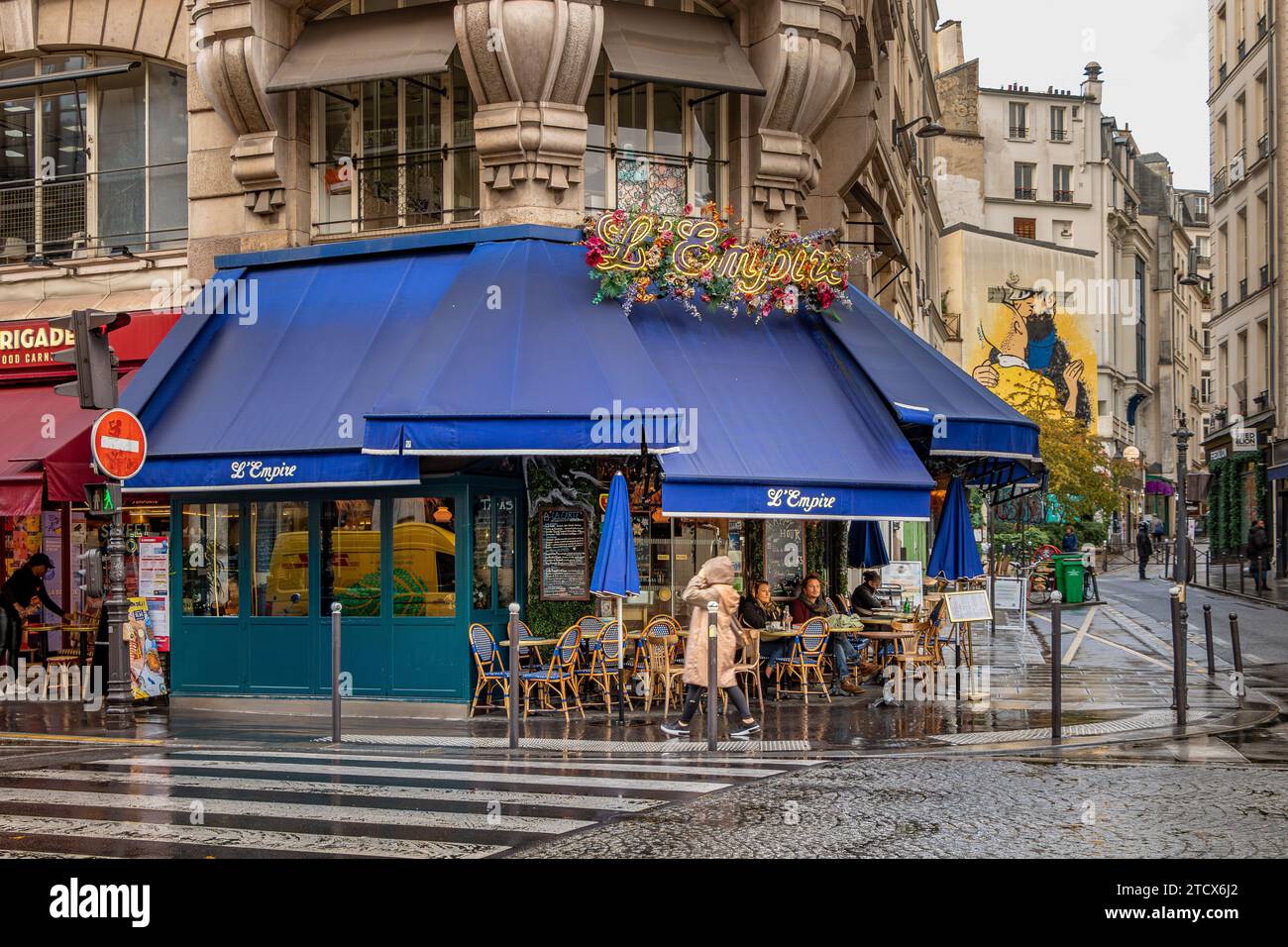 People sitting outside on the terrace at L’Empire a cafe, brasserie on Rue des Petits Carreaux on a wet rainy day in Paris, France Stock Photo