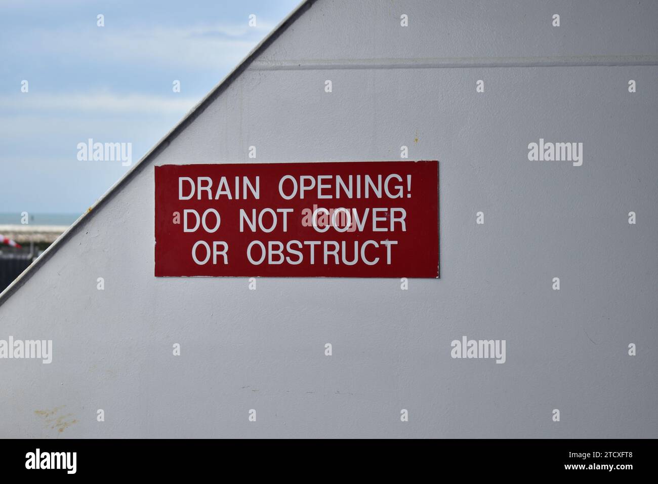 Red sign on a white metal wall on a ferry boat in the Calais car ferry port. Text says: 'Drain opening! Do not cover or obstruct' Stock Photo
