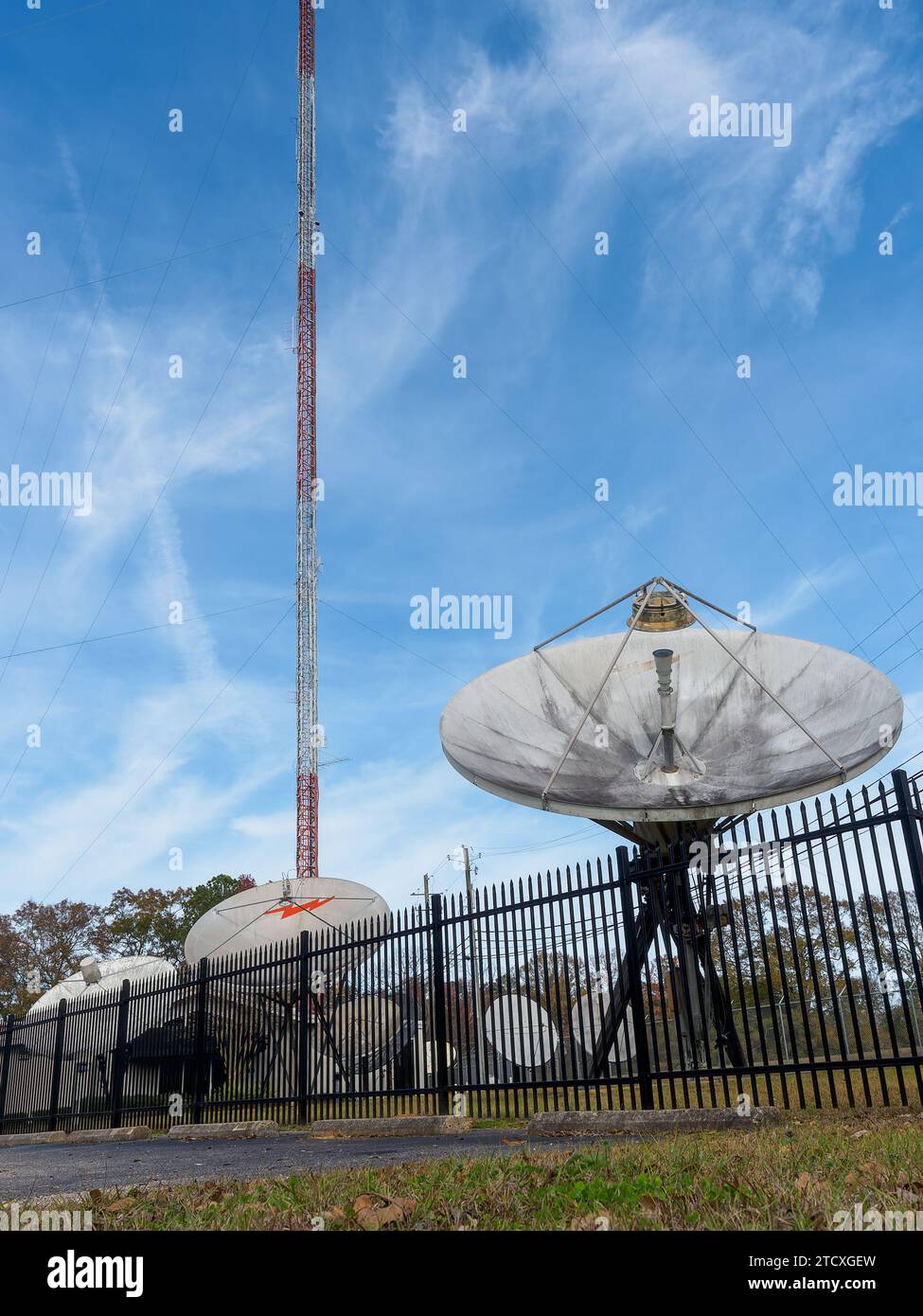 Large satellite dishes lined up under a tall television broadcasting tower or T.V. tower antenna in Montgomery Alabama, USA. Stock Photo
