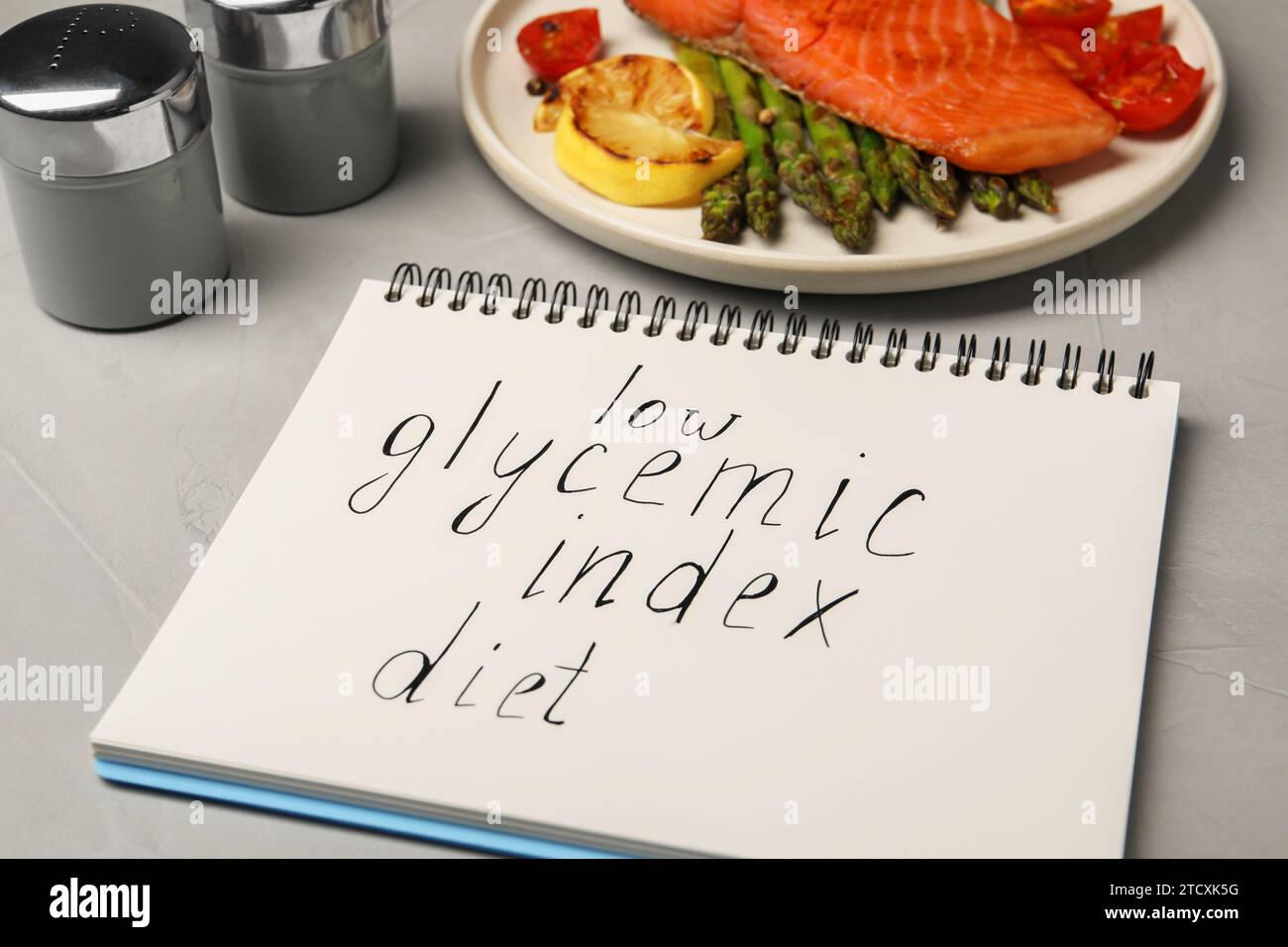 Notebook with words Low Glycemic Index Diet and plate of tasty grilled salmon on grey table Stock Photo