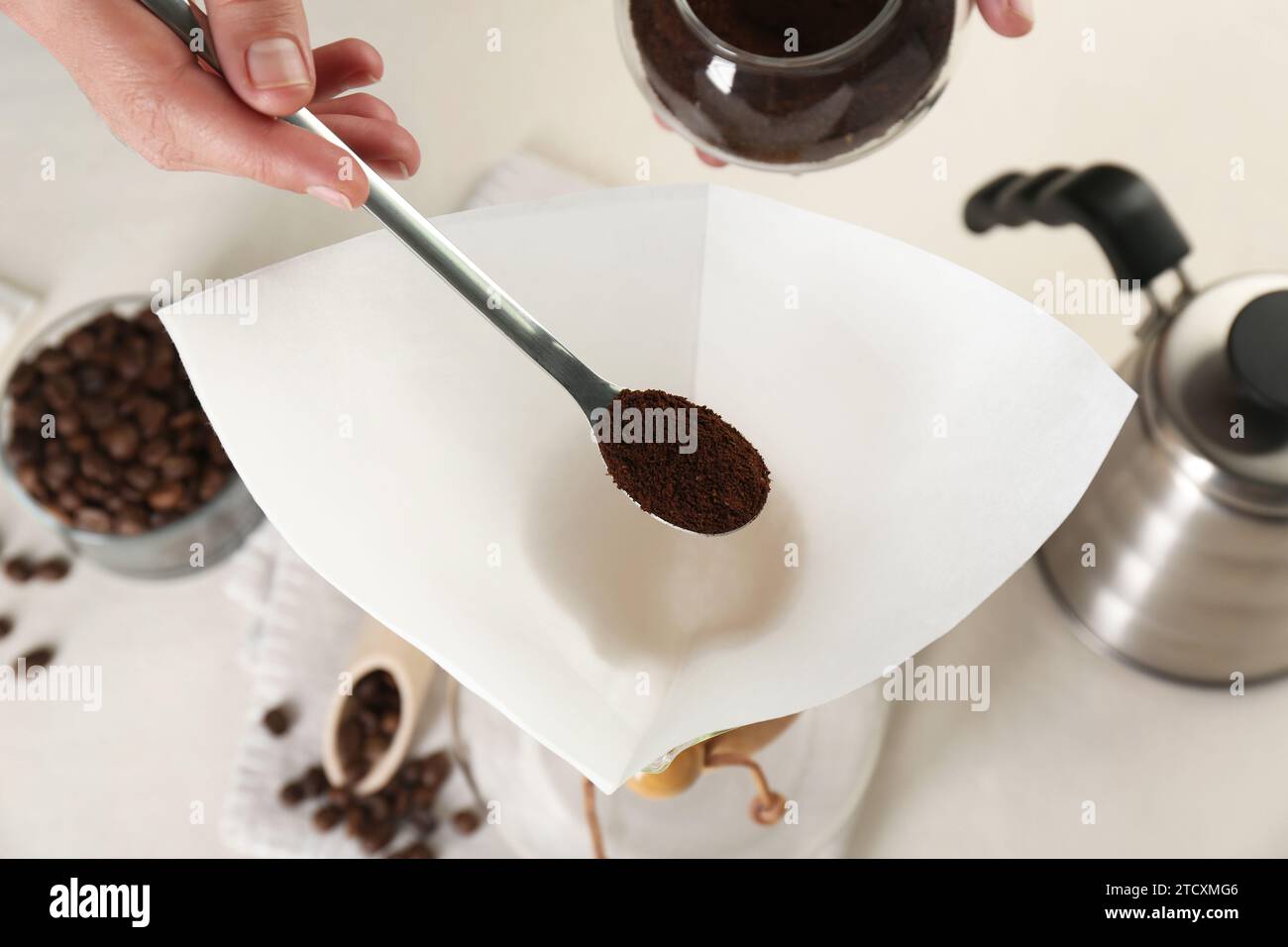 Making drip coffee. Woman adding ground coffee into paper filter at white table, closeup Stock Photo