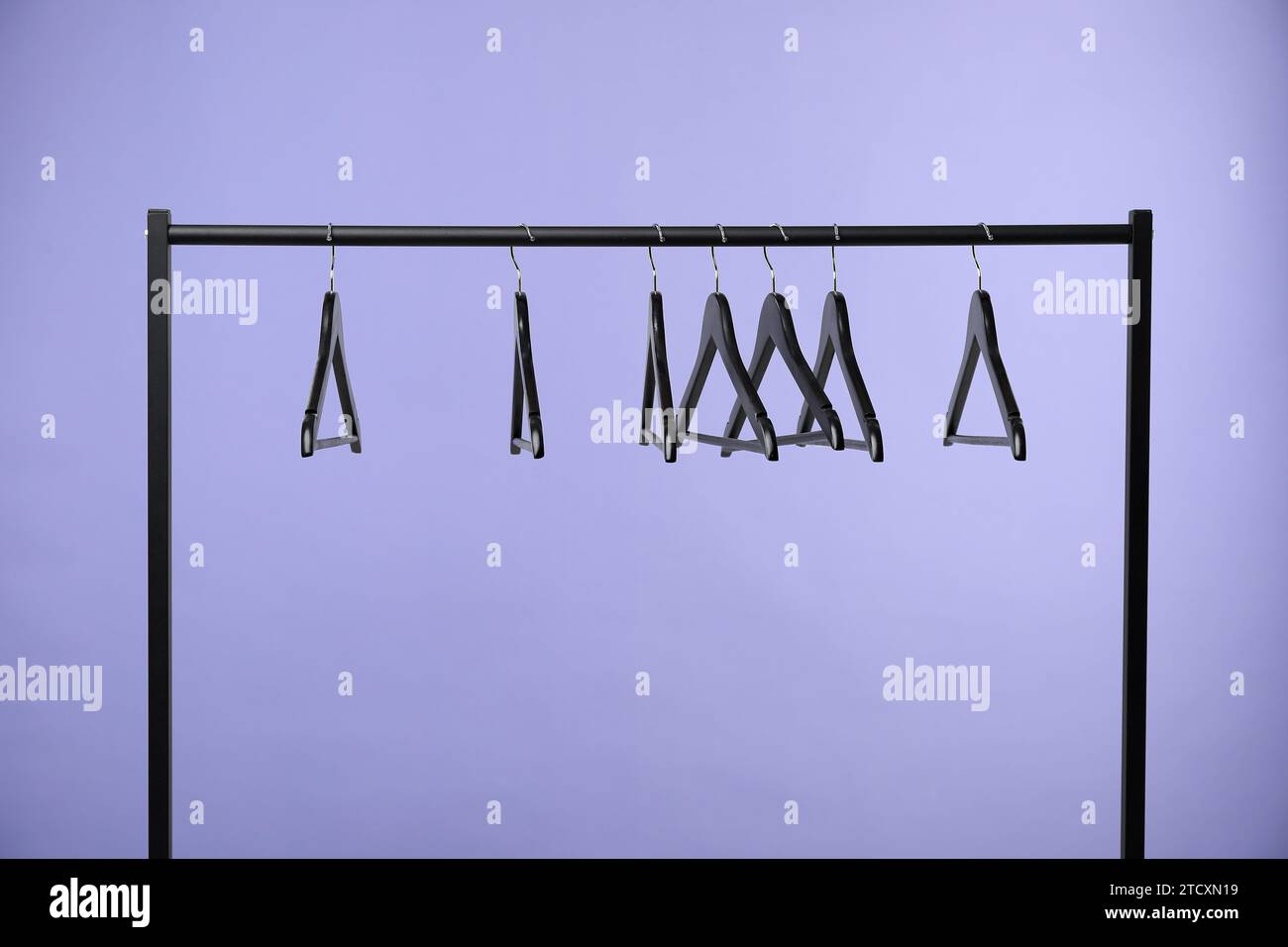 Black clothes hangers on rack against purple background Stock Photo