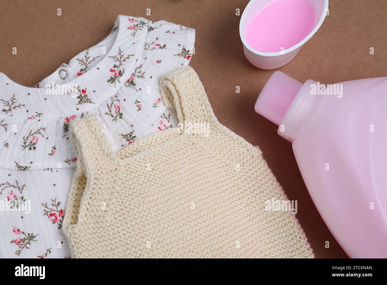 Laundry detergents and baby clothes on brown background, flat lay Stock