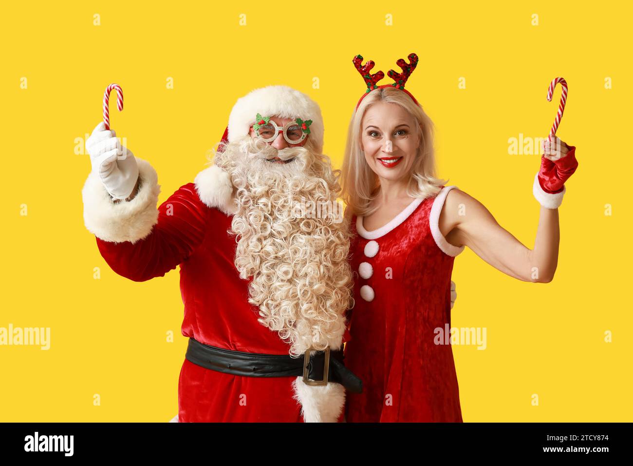 Santa and MRS Claus in Christmas deer horns with candy canes on yellow