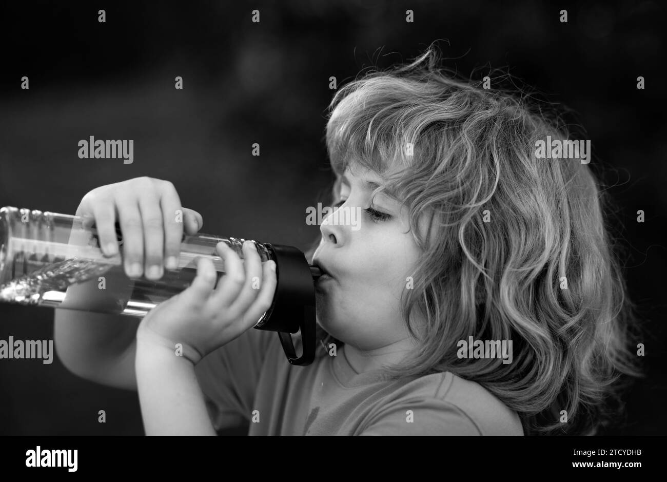 Kid drinking water outdoor. Close up portrait of boy drink water from bottle in the garden. Stock Photo