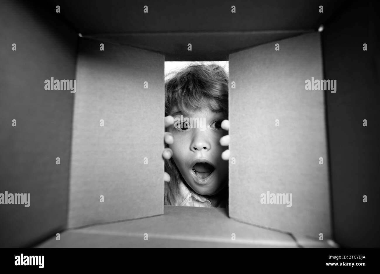 Kid opening package. Child boy age 6 year opening a carton box and looking inside, unpacking concept, surprise unboxing. Stock Photo