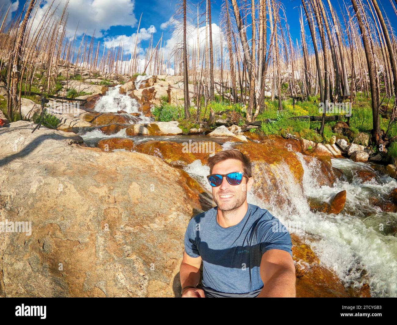 Joyful hiker takes a selfie with a striking waterfall in the regenerating forest of Rocky Mountain National Park. Stock Photo