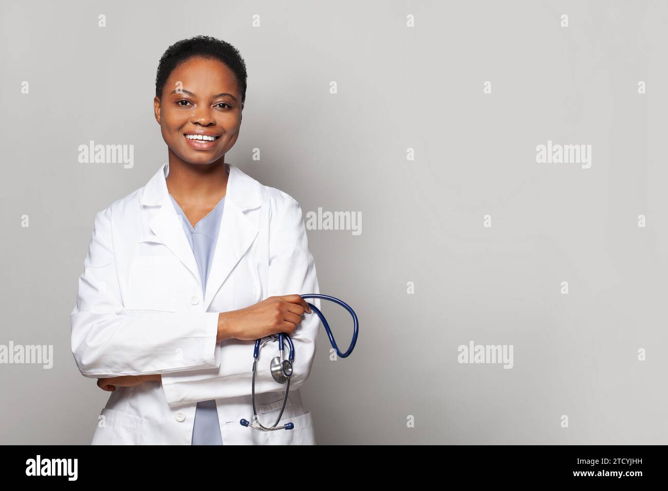 Young african american doctor woman wearing medical coat over gray background. Happy smiling nurse with crossed arms looking at the camera. Positive p Stock Photo